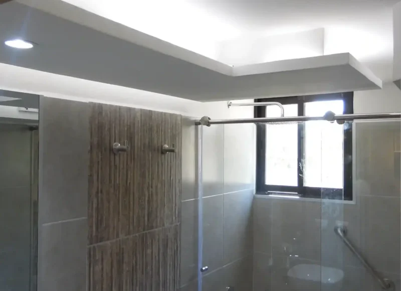 El baño tiene un diseño elegante y materiales de calidad. Las paredes de porcelanato y un lavabo de granito blanco ofrecen sofisticación. La iluminación cálida destaca los detalles y un espejo simple añade glamour. La ducha brinda una experiencia de spa, creando un lugar de relajación.